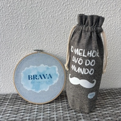 Saco tecido cinzento com texto e bastidor de madeira com logótipo sobre superfície cinzenta