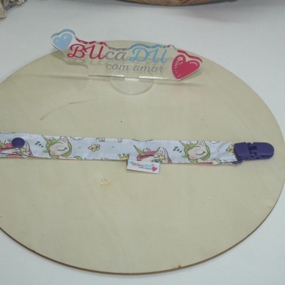 Fita para chucha com padrão de unicórnios e fecho roxo sobre base redonda de madeira