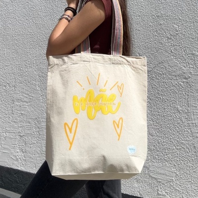 Mala de pano bege com texto amarelo e alças multicoloridas