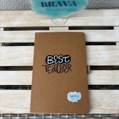 Caderno castanho com texto Best Teacher em mesa de madeira e selo Brava Estampagem