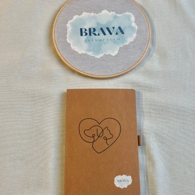 Caderno castanho com ilustração de cão e gato dentro de um coração e bordado redondo com BRAVA ESTAMPAGEM