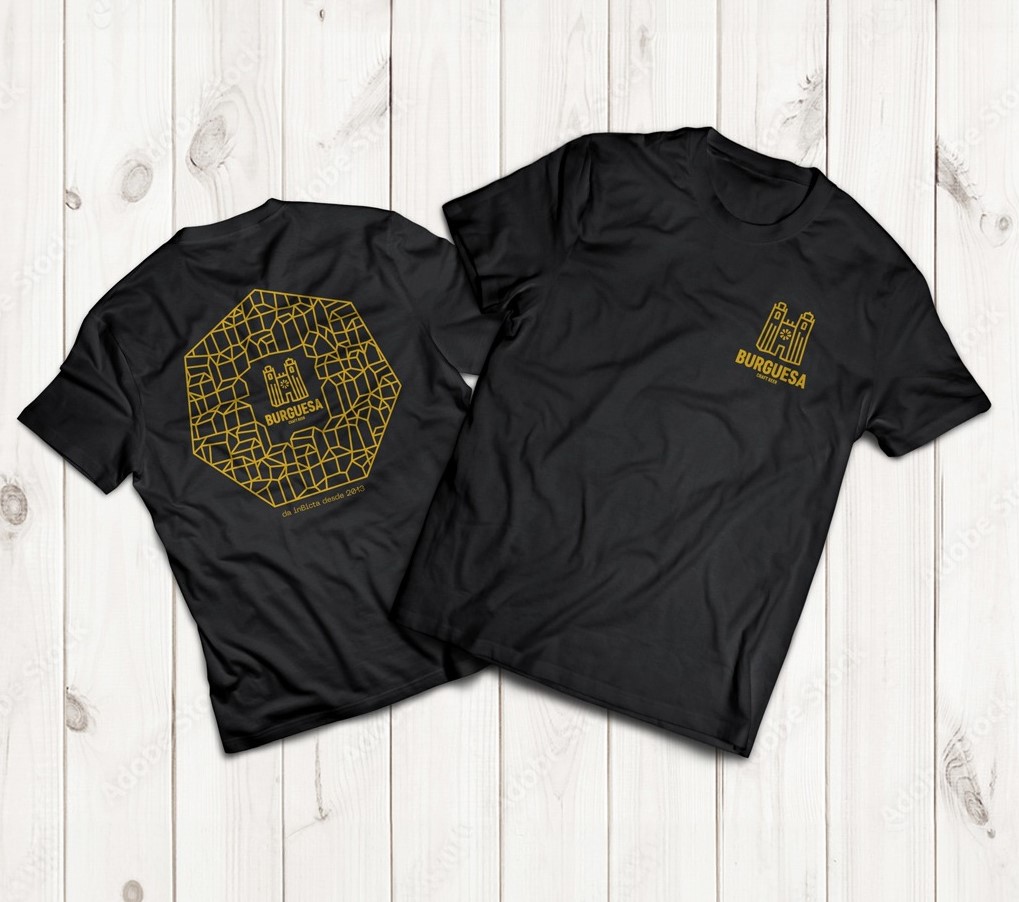 Duas t-shirts pretas com estampagem amarela do castelo e BRUGESA, sobre fundo de madeira clara