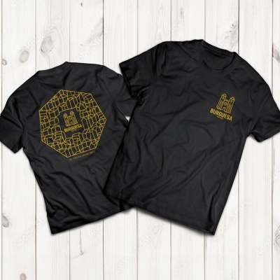 Duas t-shirts pretas com estampagem amarela do castelo e BRUGESA, sobre fundo de madeira clara