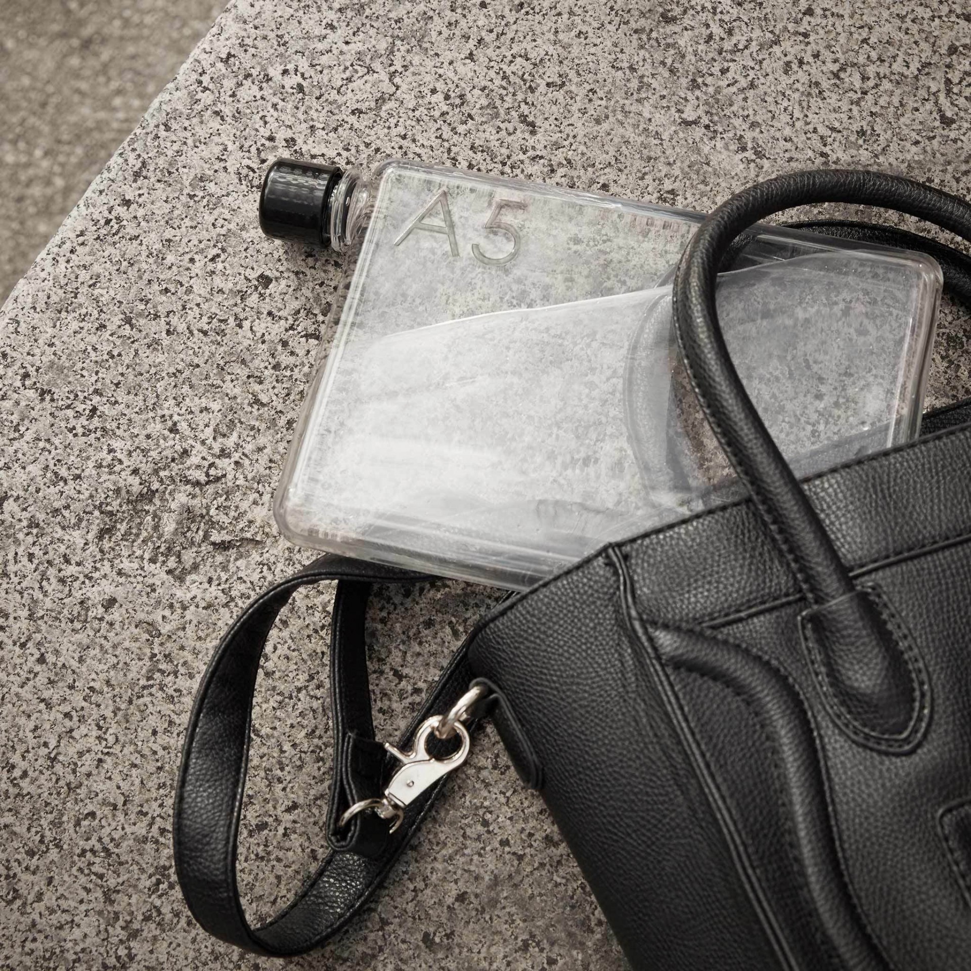 A5 memobottle Garrafa transparente A5 ao lado de bolsa preta de couro sobre superfície cinza