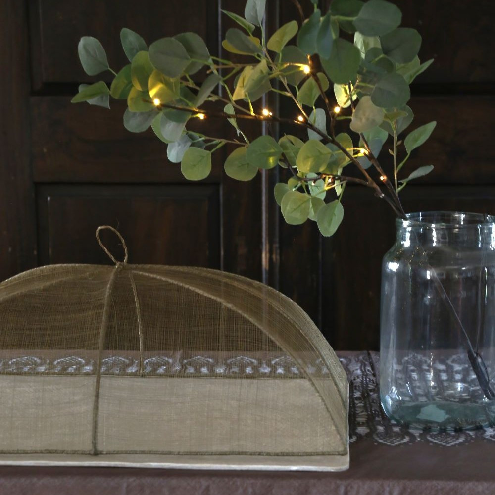 Cobertura alimentar em rede abaca 32x50x22cm - verde linho Tampa protetora de tecido bege com ramos verdes iluminados numa jarra de vidro sobre mesa