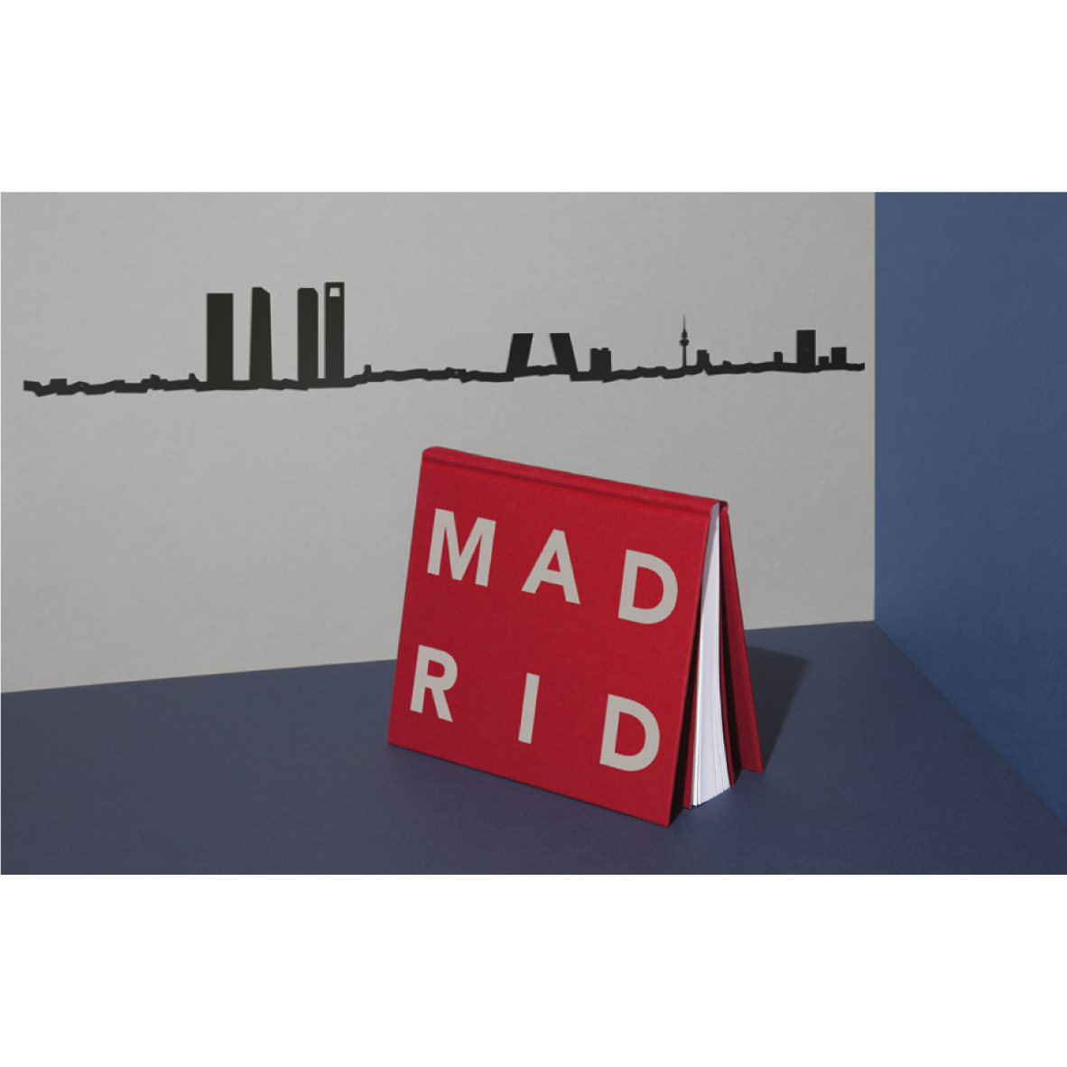 theLine® Small 50 cm - Black _ Madrid Livro vermelho com texto MADRID e silhueta preta da linha do horizonte na parede