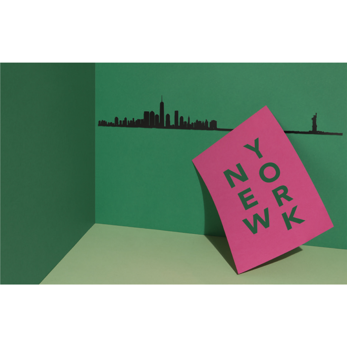 theLine® Small 50 cm - Black _ New York Cartaz rosa com texto NEW YORK sobre superfície verde e parede com silhueta de Nova Iorque.