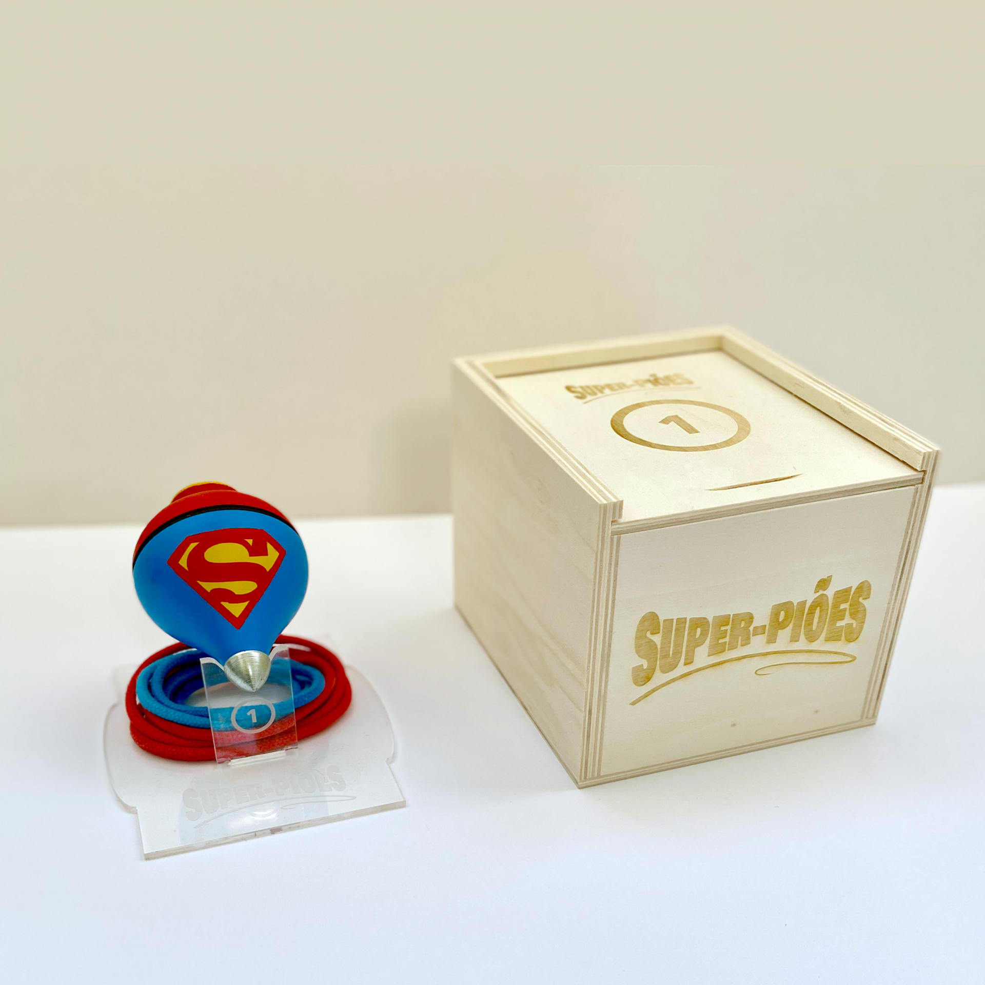 Super-Piões de Madeira Pintados à Mão SUPERMAN – Clássicos da Infância Reinterpretados por Damião Vieira Prémio de Super-Homem com caixa de madeira gravada 'Super-Piões' e número 1