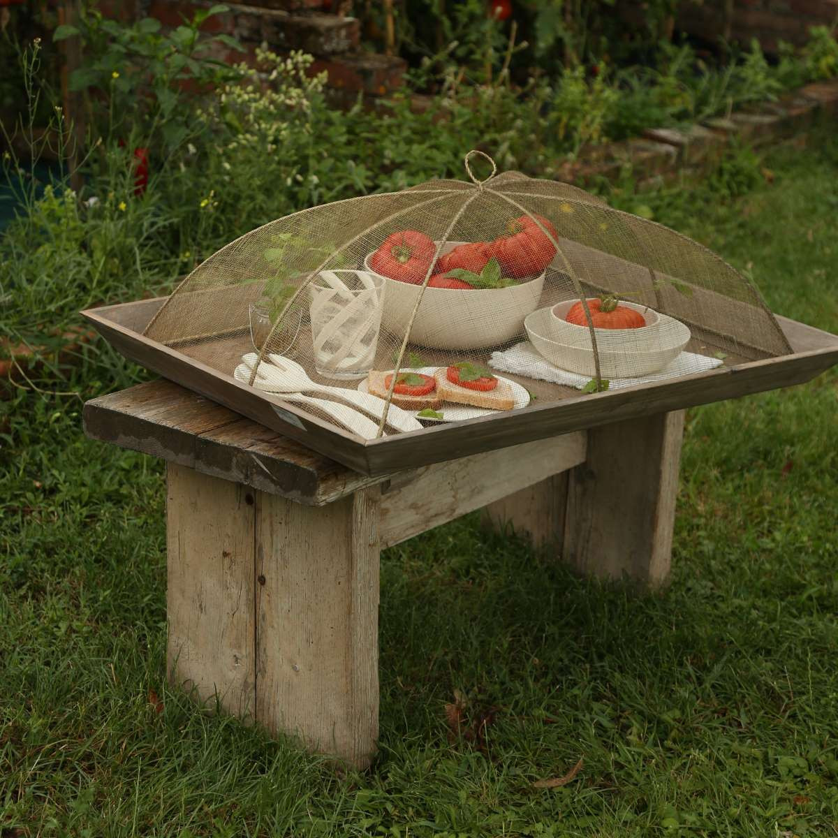 Cobertura alimentar em rede abaca 48x66x25cm - verde linho Mesa rústica com tabuleiro de madeira e rede protetora cobrindo pratos com tomates e alimentos