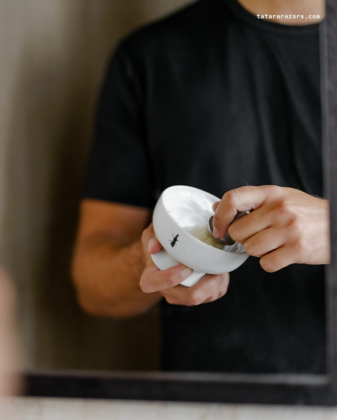 PORCELAIN SHAVING BOWL - WHITE Pessoa prepara creme de barbear em tigela branca com logótipo de formiga e pincel de barbear