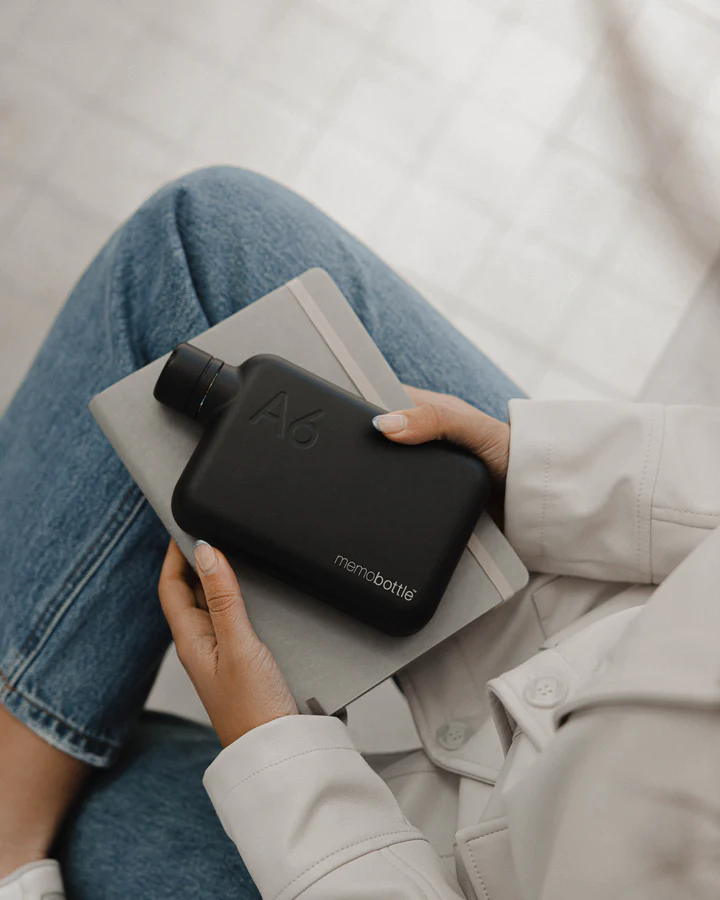 A6 memobottle Stainless Steel - BLACK Garrafa preta memobottle A6 em mãos sobre caderno cinza