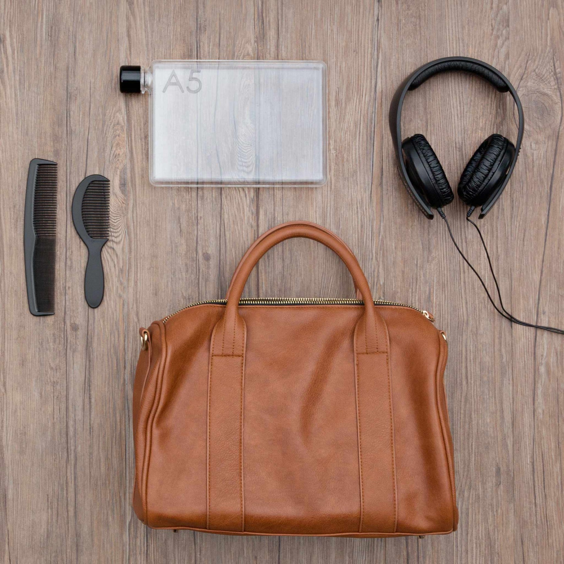 A5 memobottle Mala castanha de pele com acessórios sobre chão de madeira