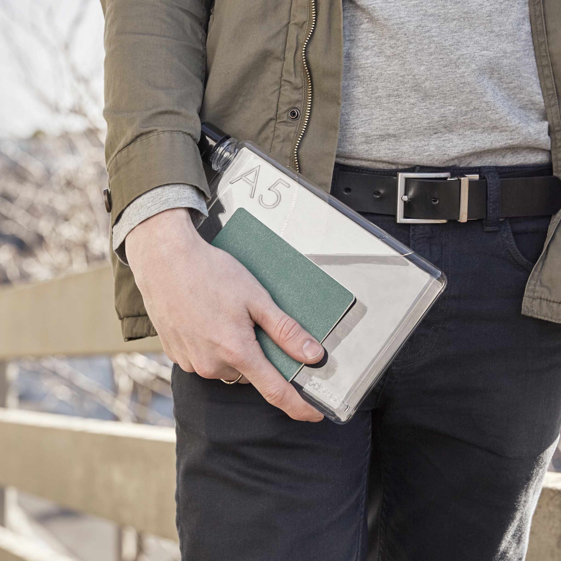 A5 memobottle Pessoa segura pasta transparente com texto A5 e caderneta verde em ambiente exterior