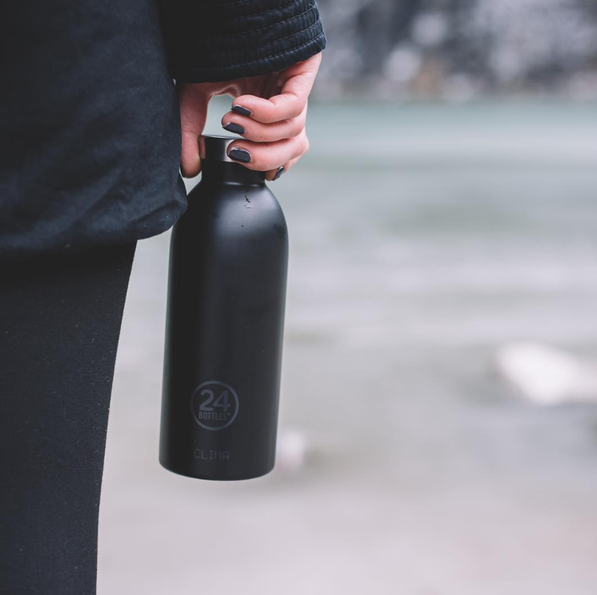 Clima Bottle - Tuxedo Black 850ml garrafa térmica preta fosca 24 BOTTLES CLIMA com tampa prateada segura pela mão de uma pessoa
