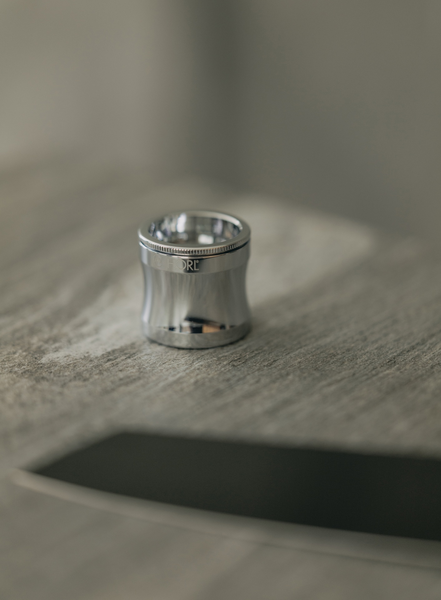 HORL MAGNIFIER Lupa metálica prateada com gravação HORL sobre uma mesa de madeira clara.