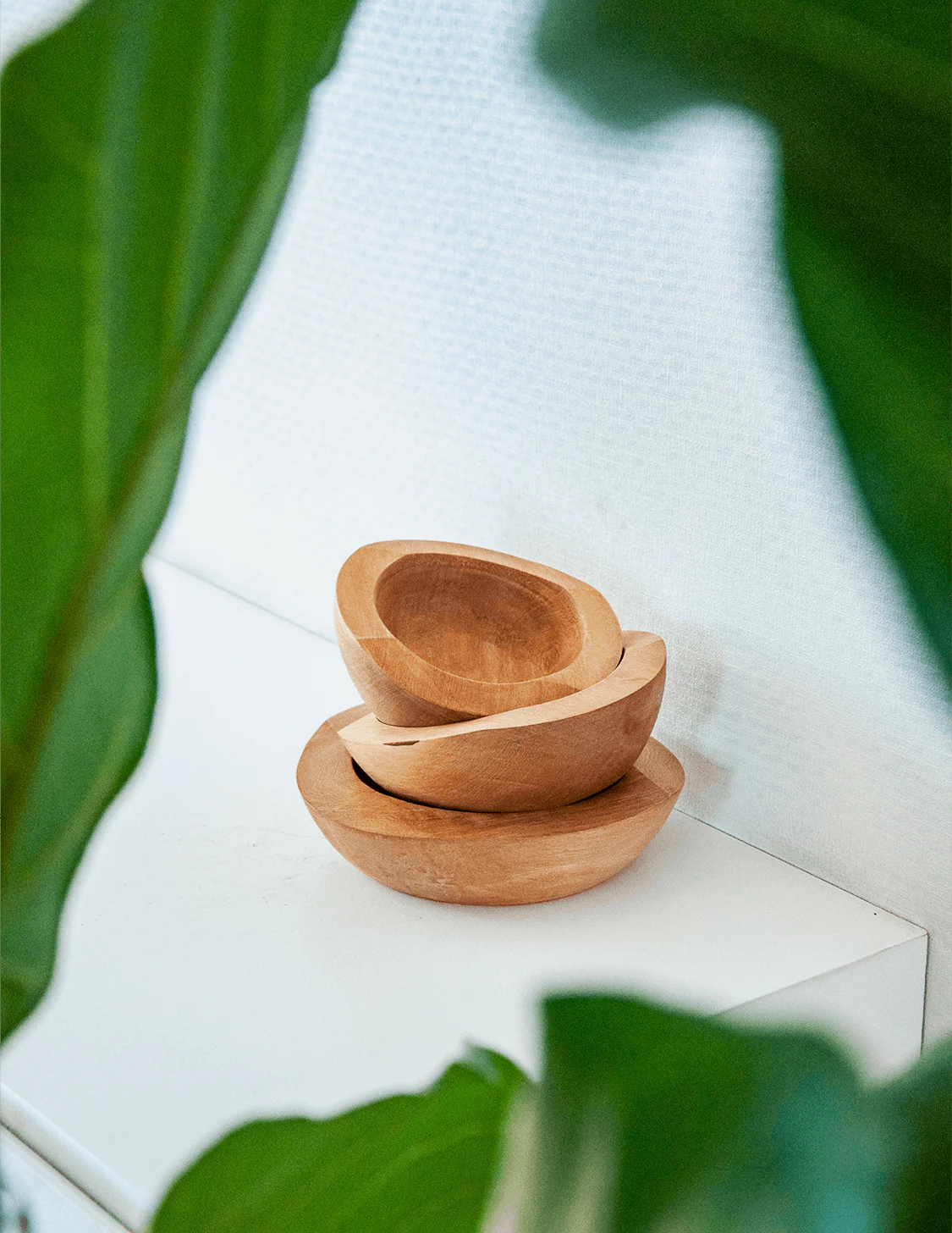 Pack IWE – Conjunto de 3 Taças em Madeira de Mañío Três tigelas de madeira empilhadas com folhas verdes ao redor.