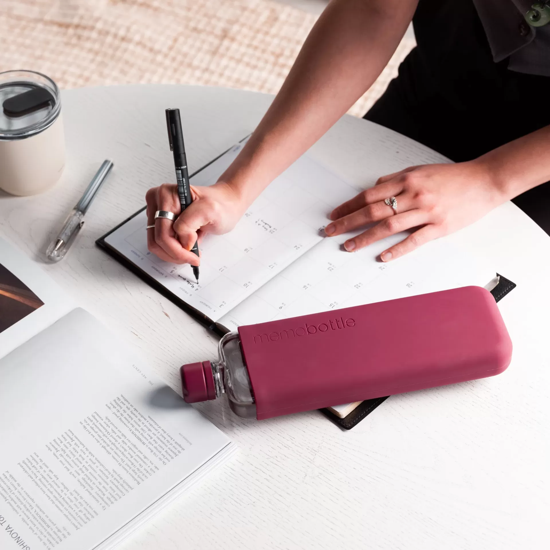 SLIM Silicone Sleeve - Wild Plum Pessoa a escrever num planner com garrafa de água rosa na mesa branca
