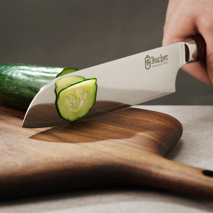 Faca Santoku Bacher em Aço Damasco com Pano de Limpeza e Cera Protetora Faca em aço cortando fatias de pepino sobre tábua de madeira