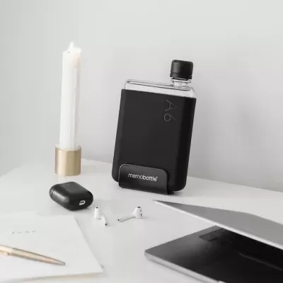 Frasco de água memobottle A6 preto sobre mesa com vela, auscultadores e portátil