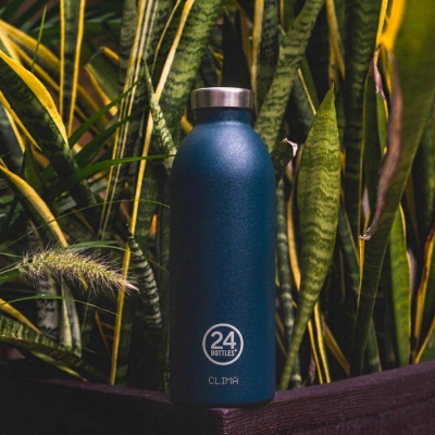 Garrafa térmica azul escura 24 BOTTLES numa varanda com plantas verdes e amarelas