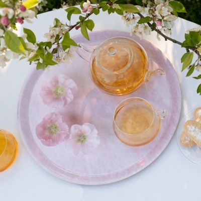 Bandeja rosa claro com flores e conjunto de chá transparente numa mesa branca com flores