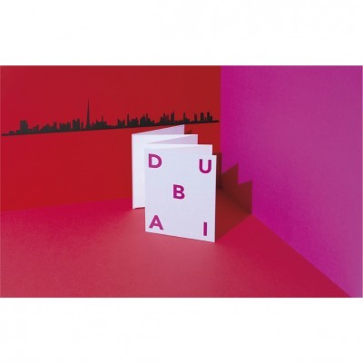 Livro branco com letras rosa a formar a palavra DUBAI em fundo vermelho e roxo com skyline preto