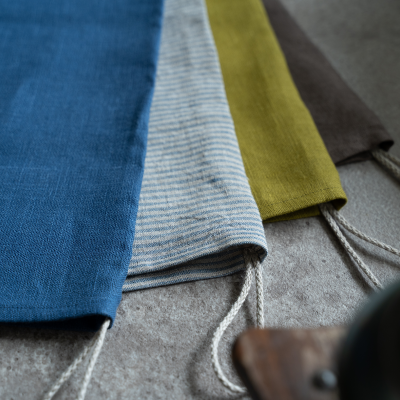 Quatro sacos de tecido coloridos com cordão, dispostos em superfície cinzenta