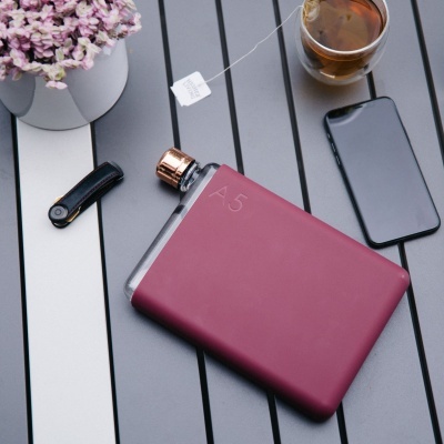 Garrafa de bolso vermelha com tampa dourada sobre mesa com chá, telefone, clipe e vaso de flores