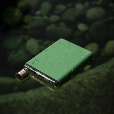 Frasco de bolso verde com gotas de água flutuando sobre água