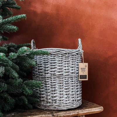 Cesto pequeno de vime branco com alças junto a árvore de Natal e fundo laranja