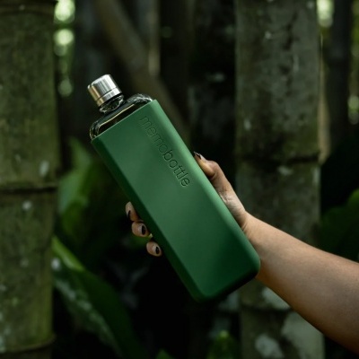 Frasco de vidro verde escuro com tampa metálica e mão segurando