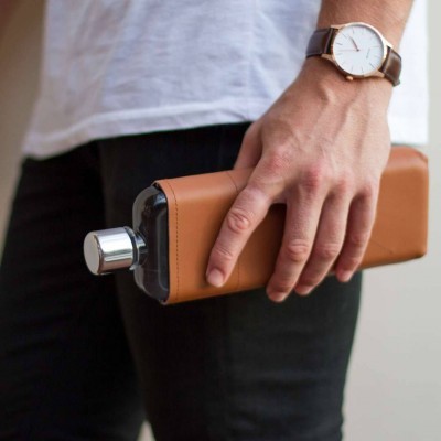 Garrafa metálica com capa de pele castanha segura por mão com relógio