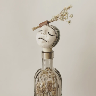 Garrafa de vidro com tampa decorativa de cabeça esculpida e flores secas
