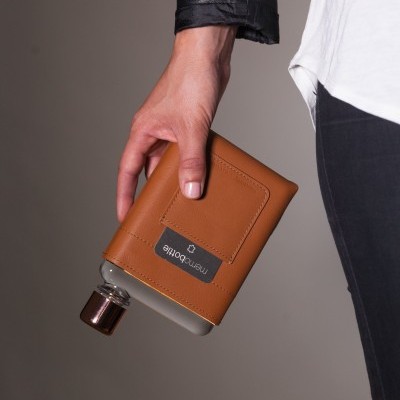 Frasco de perfume com revestimento de pele castanha segurado por mão com jaqueta preta.