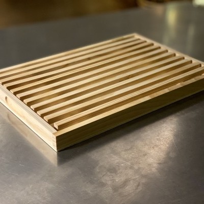 Tabuleiro de madeira clara com sulcos paralelos sobre mesa metálica cinzenta