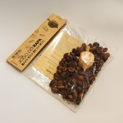 Pacote transparente com grãos de café e peça de madeira, rótulo de cartão castanho com texto em português.