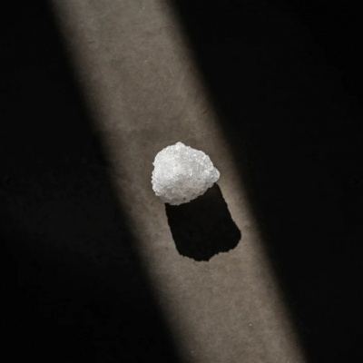 Pedra branca granular com sombra em superfície cinzenta sob feixe de luz