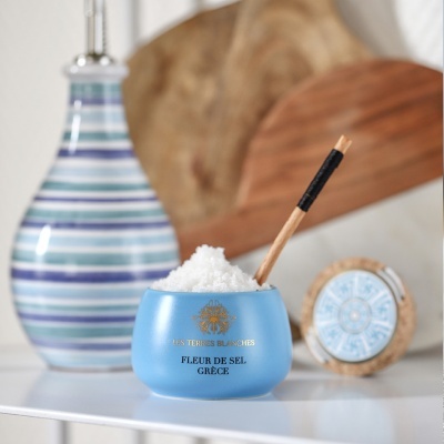 Frasco azul com flor de sal e colher de madeira, jarra cerâmica listrada e elementos de madeira ao fundo