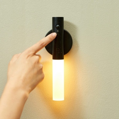 Mão a pressionar botão de candeeiro de parede preto com luz tubular opaca