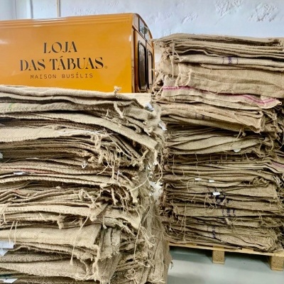 Pilha de tecidos de juta empilhados em paletes com caixa amarela ao fundo com texto