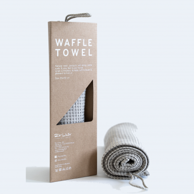 Toalha waffle cinza clara embalada em caixa de cartão castanho com texto branco