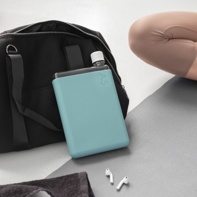 Garrafa de água azul clara A5 junto a mochila preta e auscultadores brancos sobre tapete cinzento
