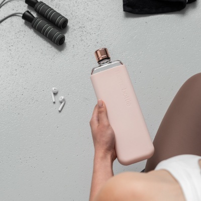 Garrafa de água rosa clara com tampa metálica na mão junto a earphones e corda de pular