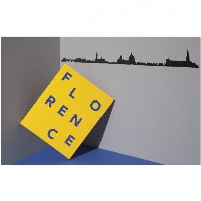 Cartaz amarelo inclinado com a palavra FLORENCE em azul e silhueta preta da linha do horizonte numa parede cinzenta