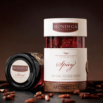 Dois frascos de molho natural de marmelo Spicy MONDEGA GOURMET com pimento African Birds Eye em rótulos brancos e castanhos, sobre superfície escura com pimentos secos