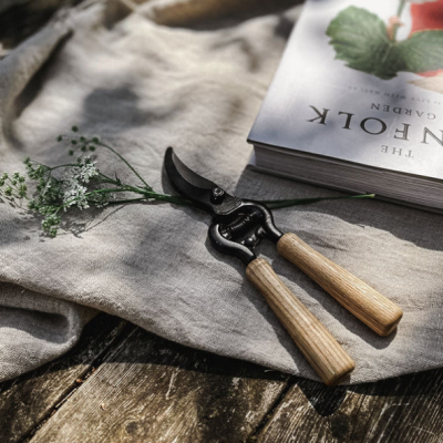 Tesoura de poda com cabos de madeira e livro 'THE KINFOLK GARDEN' sobre tecido cinza