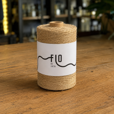 Cone de fio de juta natural com etiqueta branca FIO DE JUTA sobre mesa de madeira