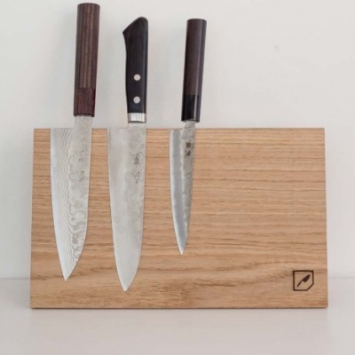Três facas com cabos de madeira e lâminas metálicas em suporte de madeira clara