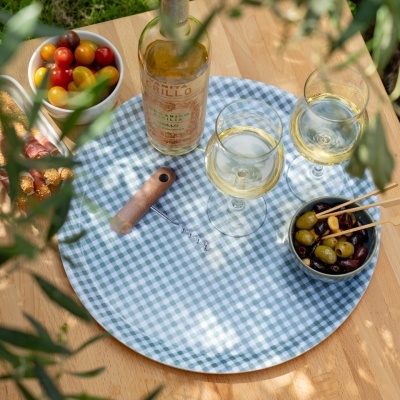 Tabuleiro redondo com vinho, taças, azeitonas e tomatinhos numa mesa de madeira