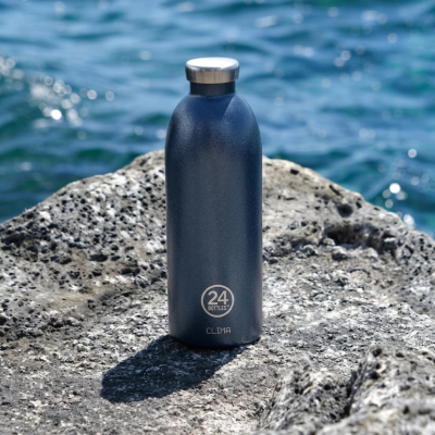 Garrafa térmica azul escura com tampa de aço inoxidável em cima de rocha junto ao mar